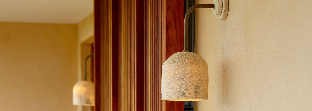 Fossil Coral Dome Arc Wall Lights by Marovo Island Traders illuminating a textured beige wall with warm light, featuring handcrafted fossil coral shades and brass fittings.