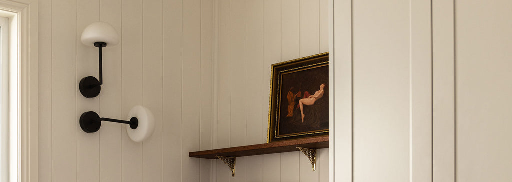 Close-up of 2 Orb Dome Long Arm Wall Light's in dark bronze, styled against white panelled walls with timber shelf and framed artwork.